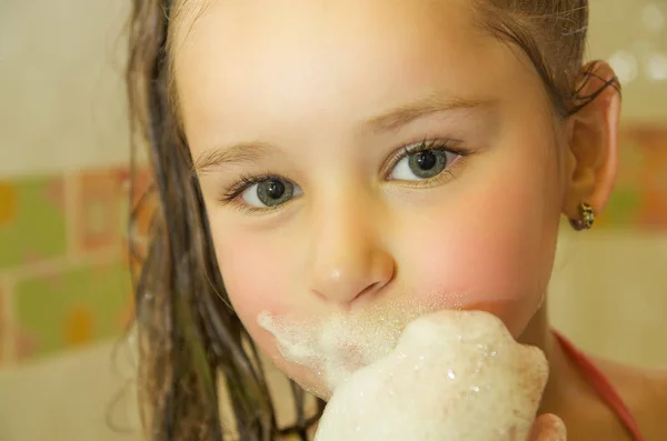 Beetje mooi meisje spelen met water en schuim met haar mond in Bad — Stockfoto