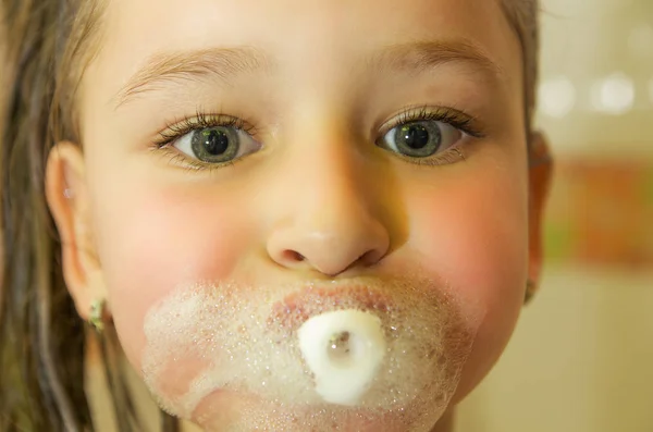 Pequeña hermosa chica jugando con agua y espuma con su boca en el baño — Foto de Stock