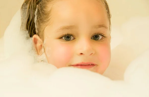 Маленькая красивая девочка играет с водой и пеной в ванной — стоковое фото