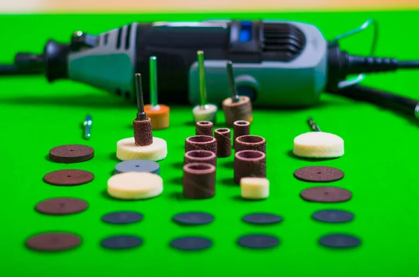 A gray drill behind of the drilling accessories on green background — Stock Photo, Image