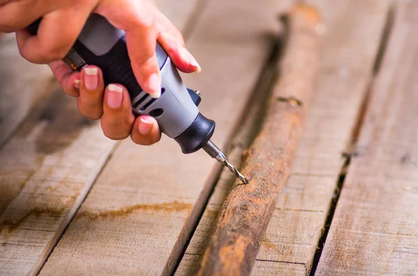 A closeup of a hardworker man drilling a wood stick with his drill on a wooden background — Stock Photo, Image