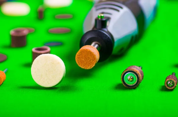 A closeup of a gray drill with some drilling accessories on green background — Stock Photo, Image