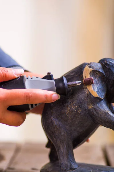 A closeup of a hardworker woman using a polisher over a wood elephant on a wooden background — Stock Photo, Image