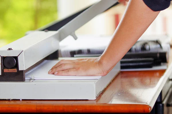 Man met handmatige papiersnijder te snijden van de rekeningen die zijn afgedrukt in de vellen papier, op een houten tafel, vervaardiging werk — Stockfoto