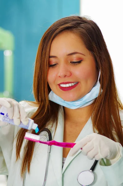 Mulher bonita paciente segurando um tothpaste em uma mão e uma escova de dentes em sua outra mão em um consultório de dentistas . — Fotografia de Stock