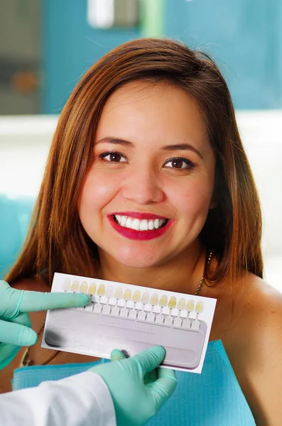 Mulher bonita paciente ter tratamento dentário no consultório dentistas enquanto ele está segurando um guia de sombra Vita dental Clássico para branqueamento e branqueamento — Fotografia de Stock