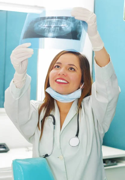 Bonita mulher feliz médico segurando um raio-X e assistindo a estrutura dos dentes no consultório de dentistas — Fotografia de Stock