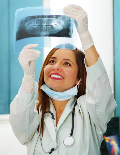 Schöne glückliche Ärztin hält ein Röntgenbild in der Hand und beobachtet die Struktur der Zähne in der Zahnarztpraxis — Stockfoto