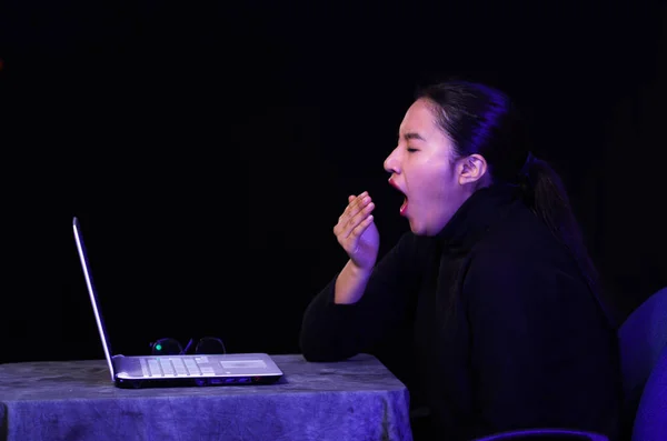 Hermosa chica vacilando dormida y bostezando delante de su computadora portátil en el fondo oscuro —  Fotos de Stock