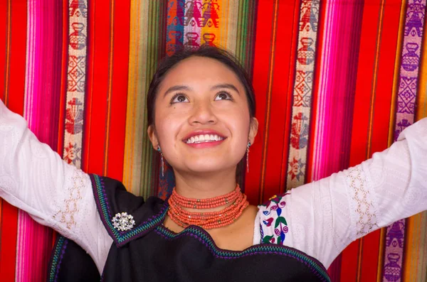 Крупный план красивой латиноамериканской модели в традиционной одежде, улыбающейся и позирующей для камеры, с цветными тканями на заднем плане — стоковое фото