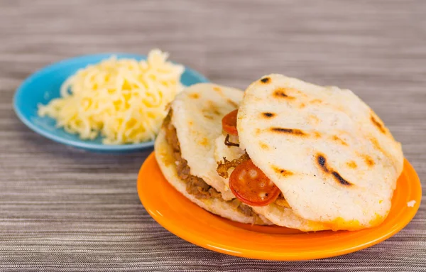 Traditional delicious arepas, shredded chicken avocado and cheddar cheese and shredded beef with grated cheese on wooden background — Stock Photo, Image