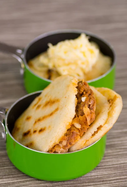 Arepas deliciosas tradicionales, aguacate de pollo rallado y queso cheddar y carne rallada dentro de una cacerola verde sobre tierra negra de madera —  Fotos de Stock