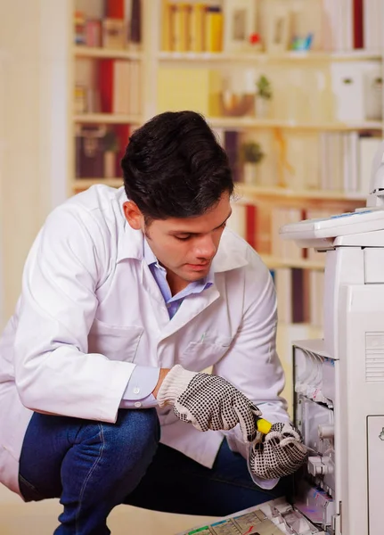 Schöner Mann, der während der Wartung mit einem Schraubenzieher einen Kopierer repariert und Arbeitshandschuhe trägt — Stockfoto