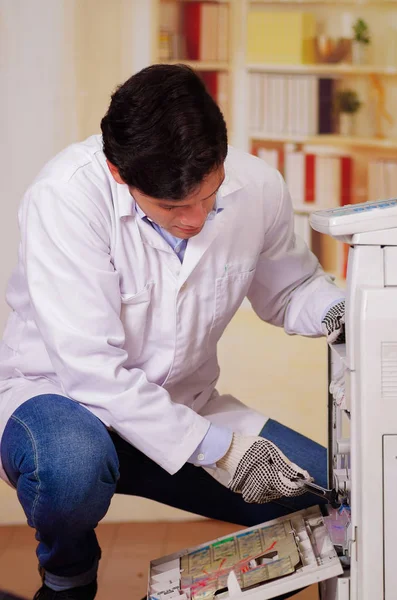 Hombre guapo arreglando una fotocopiadora durante el mantenimiento usando un destornillador con guantes de trabajo —  Fotos de Stock