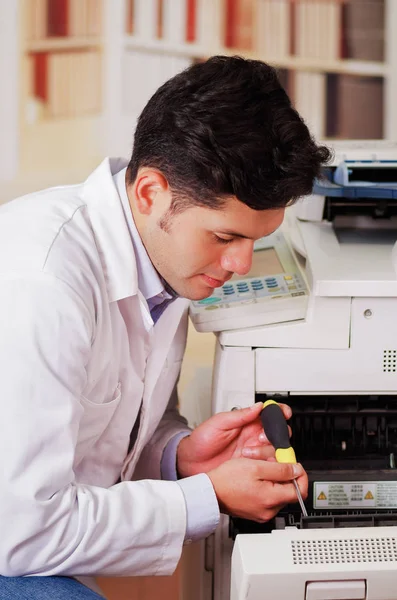 Handsome man fixing a photocopier during maintenance using a screwdriver — Stock Photo, Image