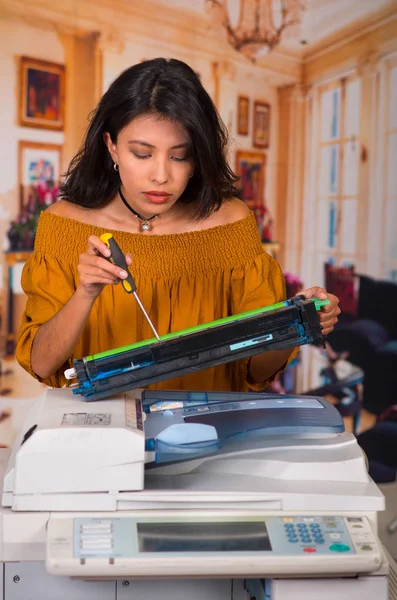 Hermosa mujer con una blusa marrón que fija una fotocopiadora durante el mantenimiento usando un destornillador —  Fotos de Stock
