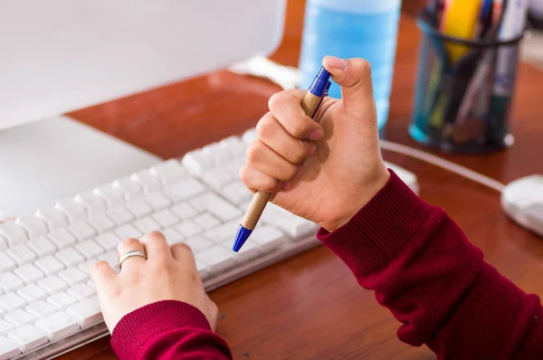 一个女的手拿着一支钢笔，在一张书桌和一台电脑的特写镜头。摆弄概念 — 图库照片
