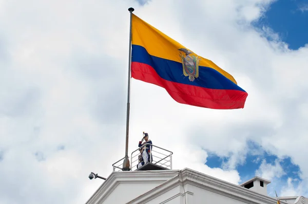 Quito, Ecuador - 27 de octubre de 2015: Un hombre no identificado en la cima del palacio presidencial durante el cambio semanal de guardias con una enorme bandera ecuatoriana — Foto de Stock