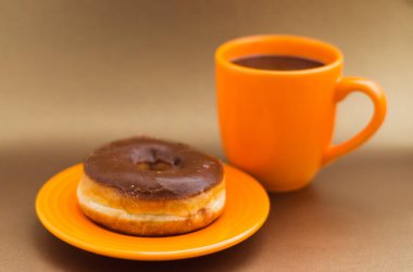 Turuncu fincan kahve yumuşak kahverengi arka planda, üstten görünüm ile turuncu bir plaka üzerinde lezzetli çörek çikolata ile sırlı