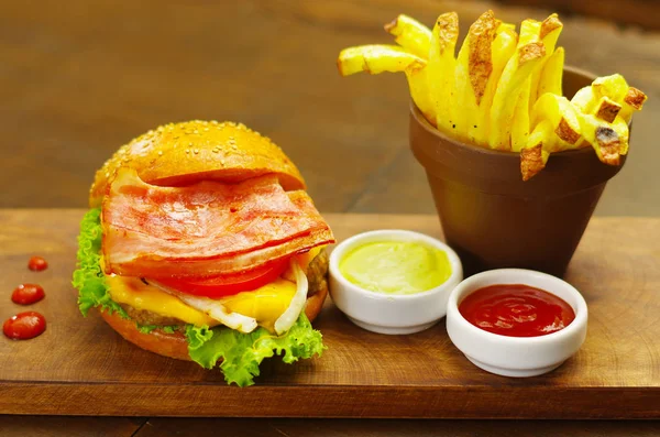 Deliciosa hamburguesa bakon con ketchup, mostaza y papas fritas sobre tabla de madera —  Fotos de Stock