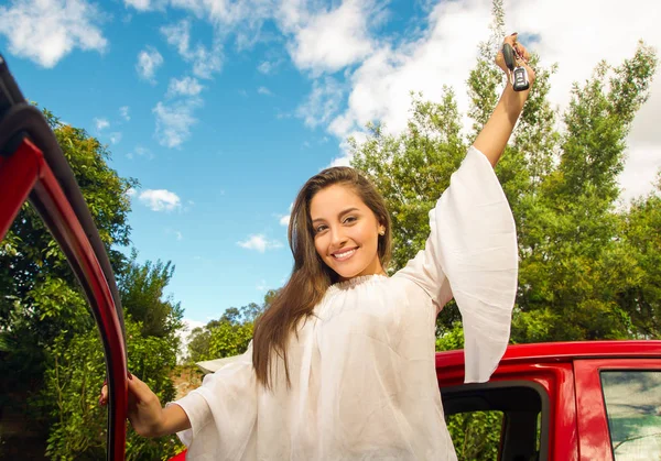 Wanita muda cantik memegang kuncinya dan tersenyum dekat mobil merahnya terbuka — Stok Foto