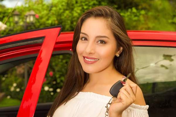 Hermosa mujer joven sexy sosteniendo sus llaves y sonriendo y un coche rojo detrás — Foto de Stock