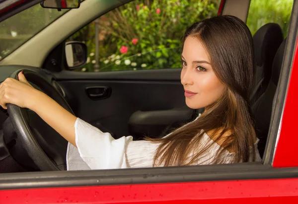 Belle femme en voiture rouge, portant un chemisier blanc pendant qu'elle conduit — Photo
