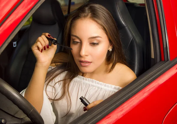 Primer plano de una hermosa joven en coche rojo usando un rímel de ojos — Foto de Stock