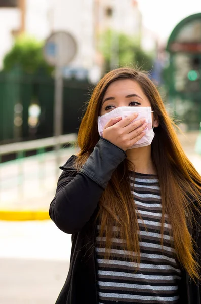 Mujer joven con su mano sobre la máscara protectora en la calle en la ciudad con la contaminación del aire, fondo de la ciudad — Foto de Stock
