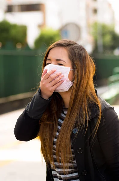 Giovane donna con maschera protettiva sentirsi male per strada in città con l'inquinamento atmosferico, sfondo della città — Foto Stock