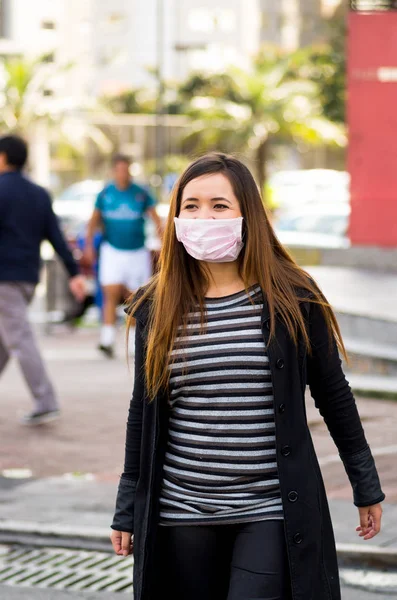 Mujer joven sonriente con máscara protectora caminando por la calle en la ciudad con contaminación del aire, fondo de la ciudad — Foto de Stock