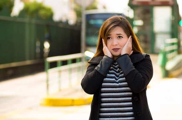 Feliz hermosa mujer joven cubriendo sus oídos con ambas manos en la calle en la ciudad con contaminación acústica con un autobús borroso detrás, fondo de la ciudad — Foto de Stock