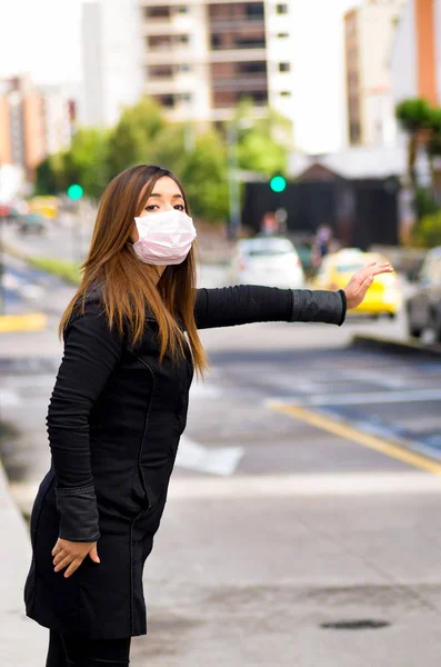 Mujer joven con máscara protectora en la calle en la ciudad con contaminación del aire, pidiendo un taxi, fondo de la ciudad — Foto de Stock