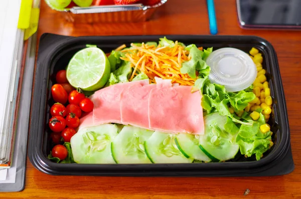 Köstlicher mediterraner Salat mit Schinken in einer Plastikbox auf einem Holztisch — Stockfoto