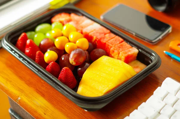 Nahaufnahme eines gesunden Frühstücks, Obstsalat in Plastikbox auf Holztisch verpackt — Stockfoto