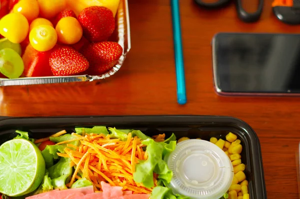 Nahaufnahme eines köstlichen frischen Salats im mediterranen Stil mit Schinken und Obst sal in einer Plastikbox auf einem Holztisch — Stockfoto