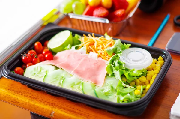 Köstlicher mediterraner Salat mit Schinken in einer Plastikbox auf einem Holztisch — Stockfoto