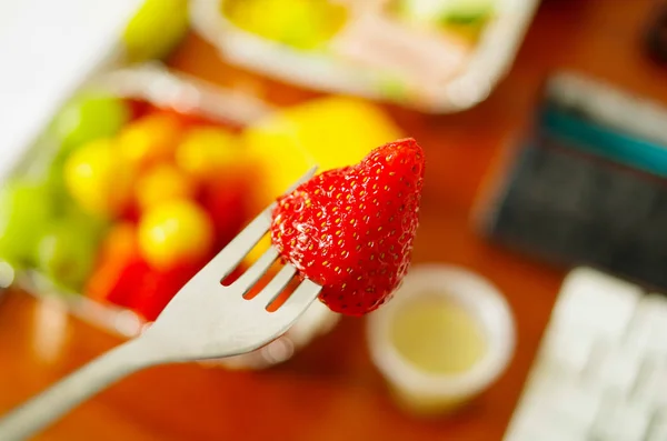 Healthy man using a white plastic fork to eat in the office a delicious raspberry with a blurred background — Stock Photo, Image