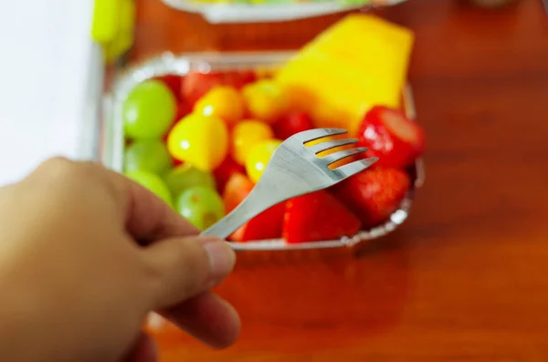 Gesunder Mann mit Gabel, um im Büro einen köstlichen frischen Obstsalat auf Aluminiumbox auf Holztisch über der Ansicht zu essen — Stockfoto