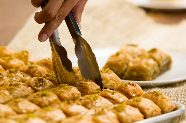 Close up of a man using a Bakery clamps to take a baklava food, traditional turkish food with pistachio — Stock Photo, Image