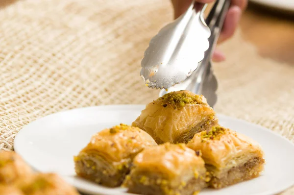 Close up of a man using a Bakery clamps to take a baklava food, traditional turkish food with pistachio — Stock Photo, Image