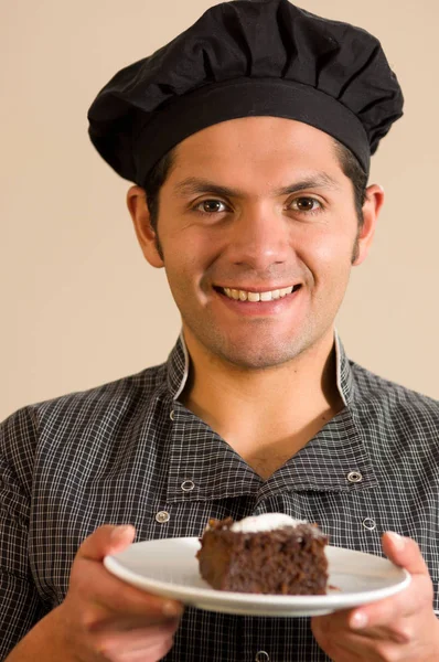 Красивый улыбающийся мужчина держит кусок темного шоколадного торта на мягком коричневом фоне — стоковое фото