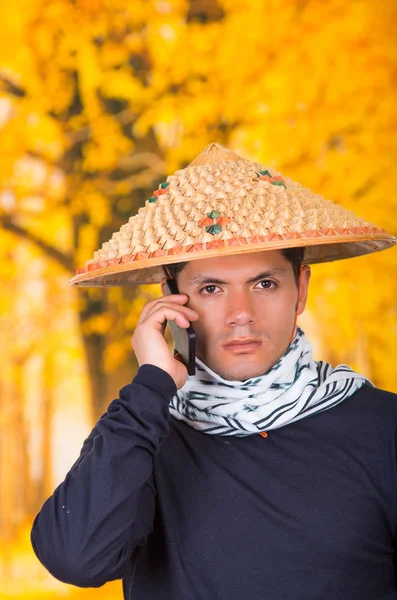 Portrait of a handsome hispanic young business guy wearing an asian conical hat and a scarf around his neck using his cellphone in autum background — Stock Photo, Image