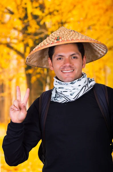 Портрет красивого латиноамериканца, молодого бизнесмена в азиатской конической шляпе и подающего знак победы на заднем плане осени — стоковое фото