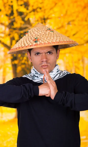 Retrato de un joven hombre de negocios hispano guapo con un sombrero cónico asiático haciendo un saludo tradicional con las manos en el fondo del autum —  Fotos de Stock