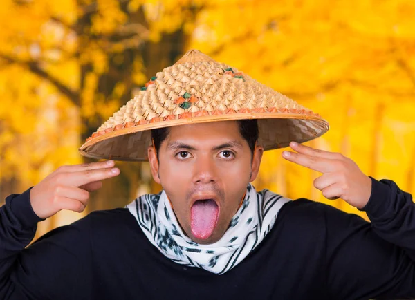 Close up van een knappe Spaanse jonge bedrijf man met een Aziatische conische hoed doet een gek gezicht en neem uit de tong in autum achtergrond — Stockfoto