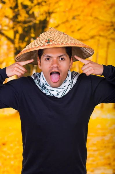 英俊的西班牙裔年轻商务肖像家伙穿着做个可笑的鬼脸亚洲圆锥形的帽子，拿出舌头在秋天背景 — 图库照片