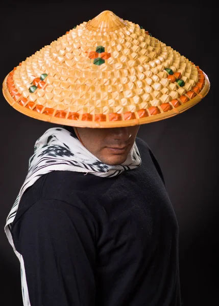 Retrato de un joven hombre de negocios hispano guapo usando un sombrero cónico asiático y escondiendo su cara con el sombrero, en fondo negro —  Fotos de Stock