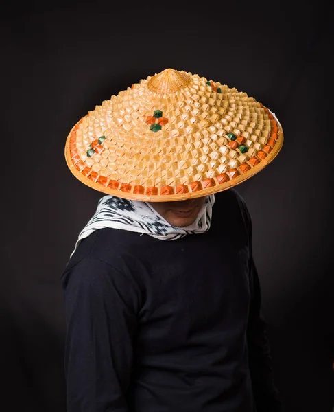 Retrato de un joven hombre de negocios hispano guapo usando un sombrero cónico asiático y escondiendo su cara con el sombrero, en fondo negro —  Fotos de Stock