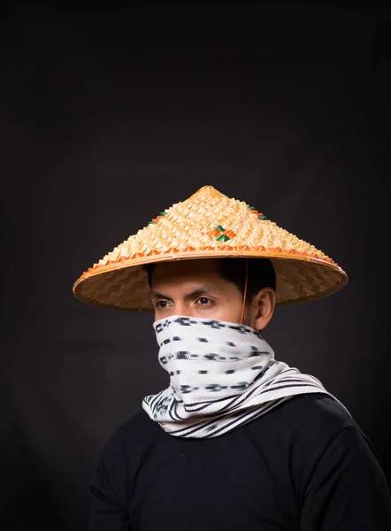 Retrato de un joven hombre de negocios hispano guapo con un sombrero cónico asiático y escondiendo su cara con una bufanda en fondo negro —  Fotos de Stock